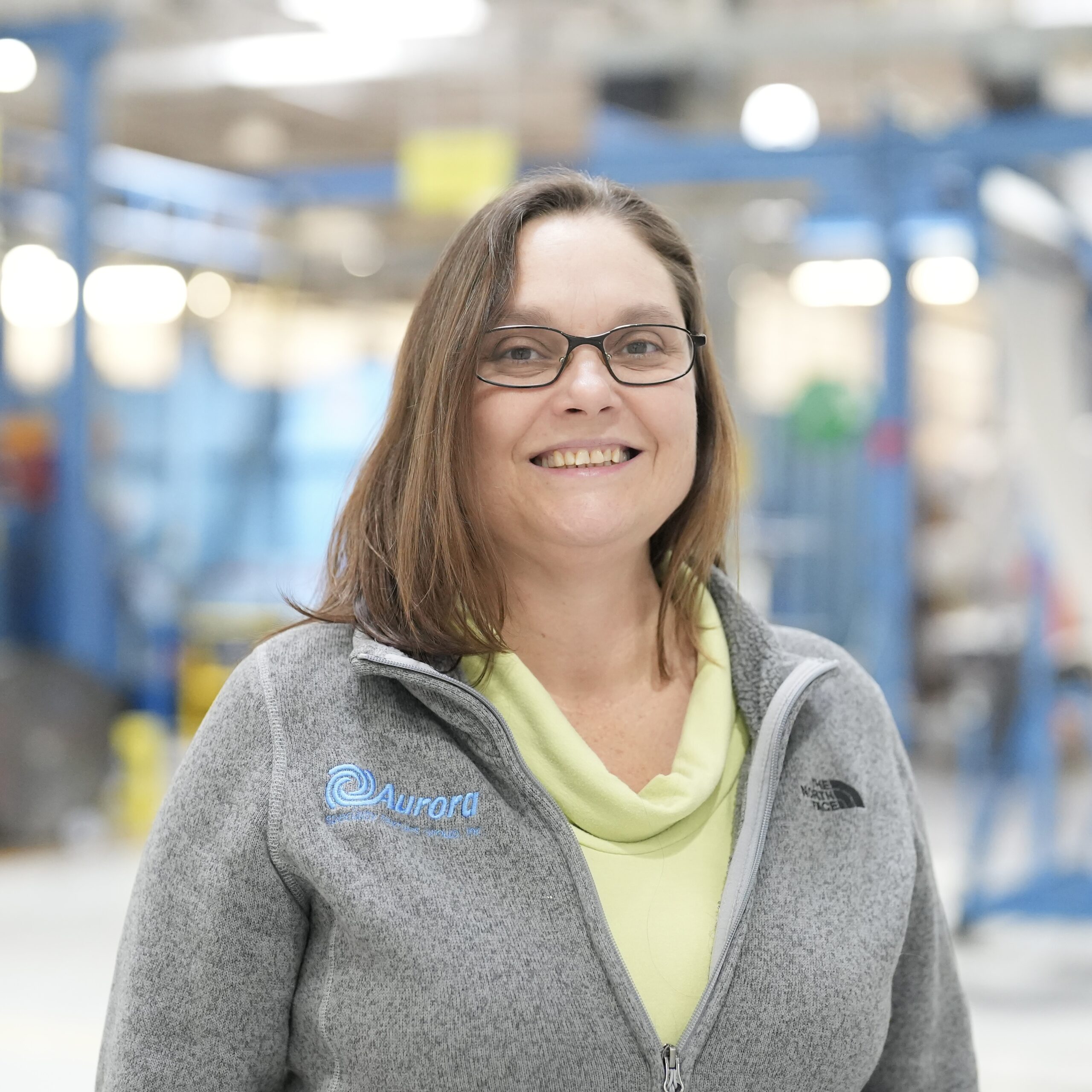 Smiling woman in gray jacket and glasses indoors.